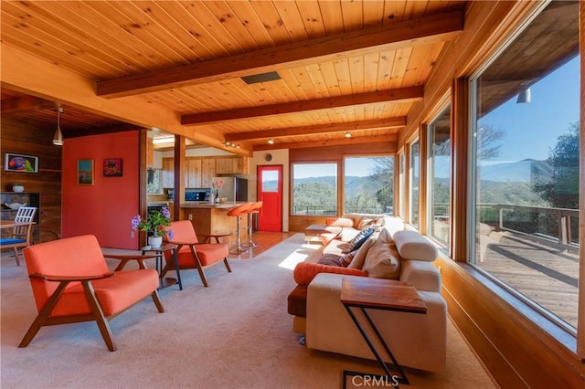 carpeted living room with wooden walls, wooden ceiling, a mountain view, and beam ceiling