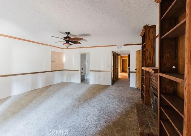 spare room with a textured ceiling, crown molding, dark colored carpet, and ceiling fan