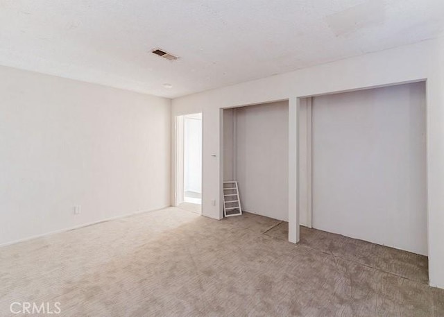 unfurnished bedroom featuring visible vents, carpet flooring, and two closets