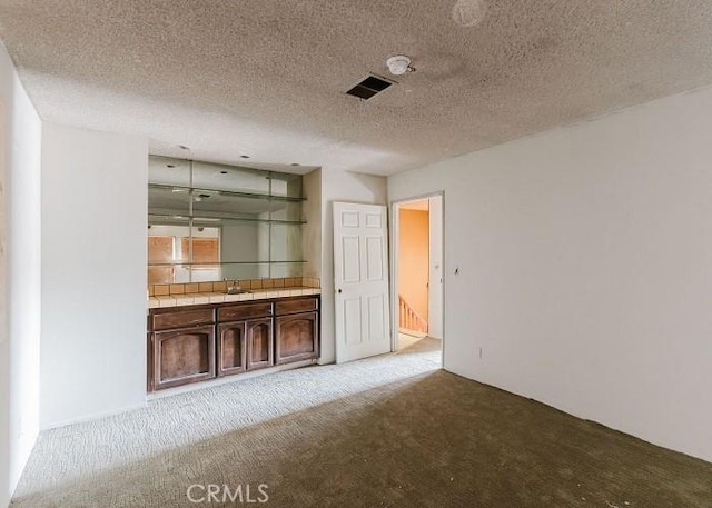 interior space featuring sink, tile counters, light colored carpet, dark brown cabinetry, and a textured ceiling