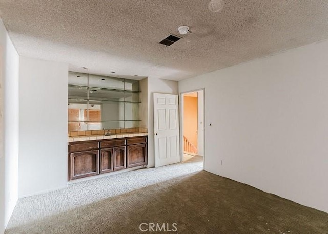 bar featuring a textured ceiling, carpet flooring, visible vents, and a sink