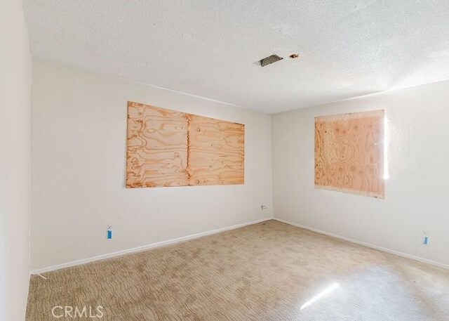 carpeted spare room featuring baseboards and a textured ceiling