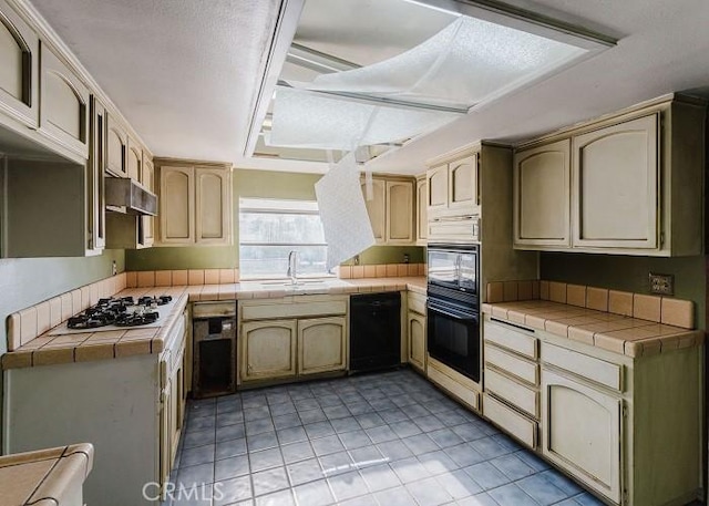 kitchen with black appliances, a sink, under cabinet range hood, tile countertops, and light tile patterned flooring