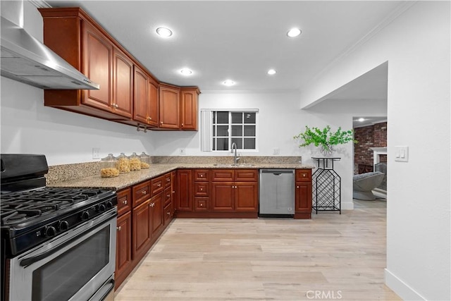 kitchen featuring wall chimney range hood, sink, stainless steel appliances, light stone countertops, and a brick fireplace