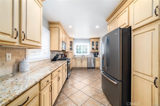 kitchen with light tile patterned flooring, tasteful backsplash, light brown cabinets, stainless steel appliances, and light stone countertops