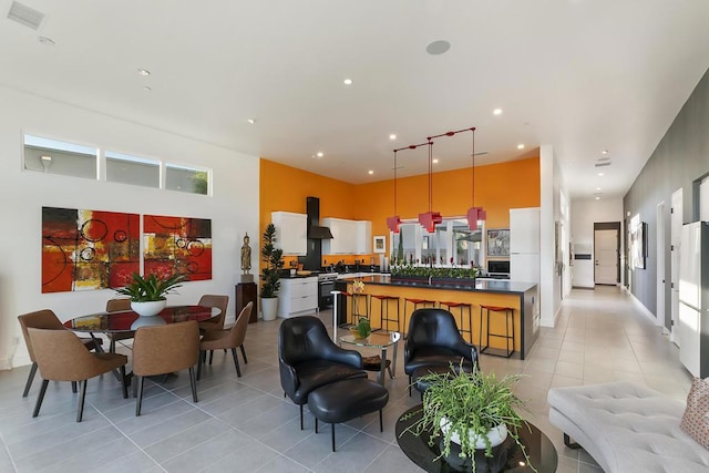 kitchen featuring white cabinetry, decorative light fixtures, a center island, light tile patterned floors, and wall chimney range hood