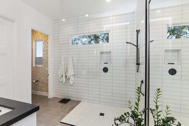 bathroom with tile patterned flooring, vanity, a healthy amount of sunlight, and a tile shower