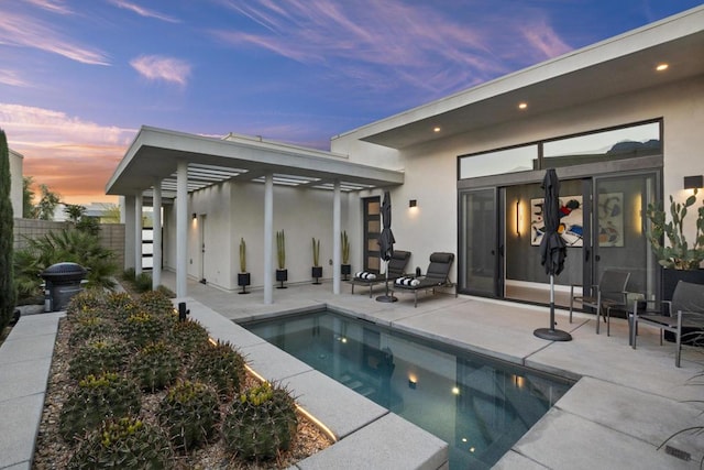 back house at dusk featuring a fenced in pool and a patio