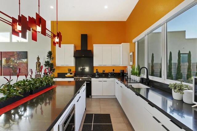 kitchen featuring light tile patterned flooring, high end stove, sink, white cabinets, and wall chimney exhaust hood