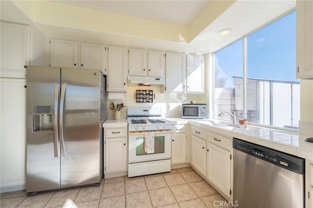 kitchen featuring stainless steel appliances, tile counters, white cabinets, light tile patterned flooring, and under cabinet range hood