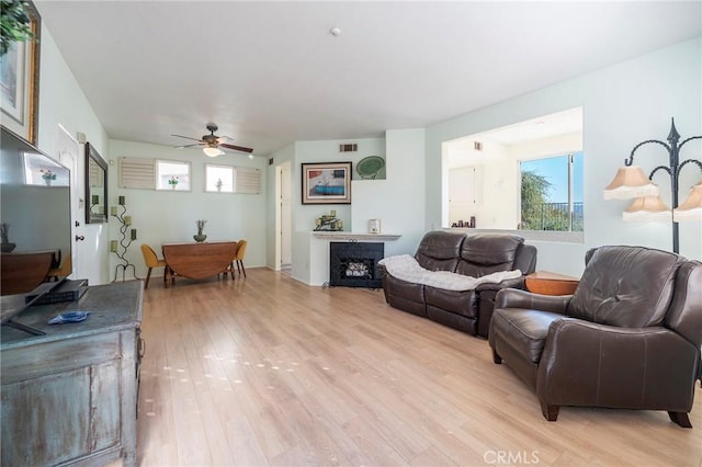 living room with light wood-type flooring, visible vents, a fireplace, and ceiling fan