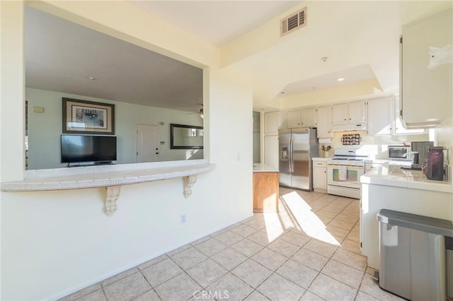 kitchen with visible vents, white cabinets, appliances with stainless steel finishes, tile counters, and a tray ceiling