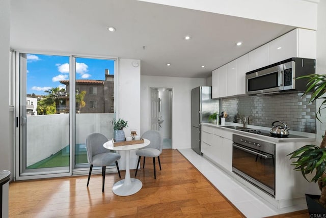 kitchen with light hardwood / wood-style flooring, appliances with stainless steel finishes, backsplash, expansive windows, and white cabinets