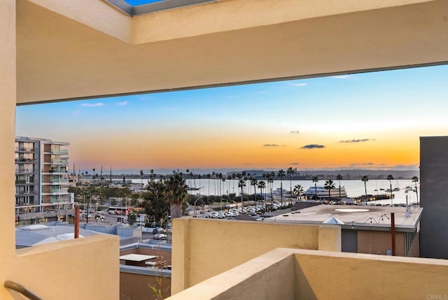 balcony at dusk featuring a water view