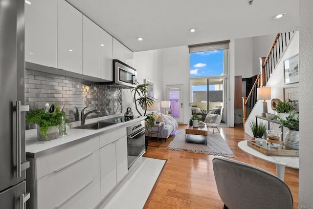 kitchen with sink, appliances with stainless steel finishes, backsplash, light hardwood / wood-style floors, and white cabinets