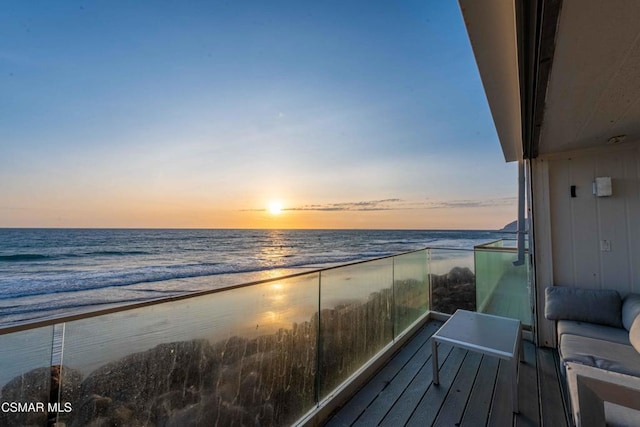 balcony at dusk featuring a water view and a view of the beach