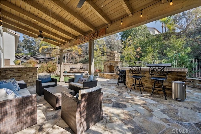 view of patio featuring ceiling fan, an outdoor living space with a fireplace, and an outdoor bar