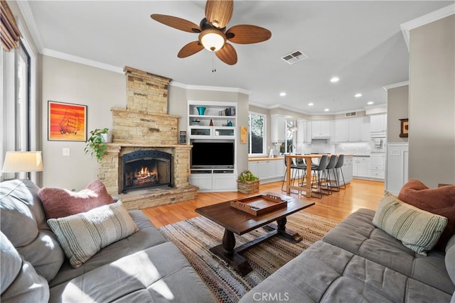 living room featuring crown molding, light hardwood / wood-style flooring, ceiling fan, a fireplace, and built in shelves