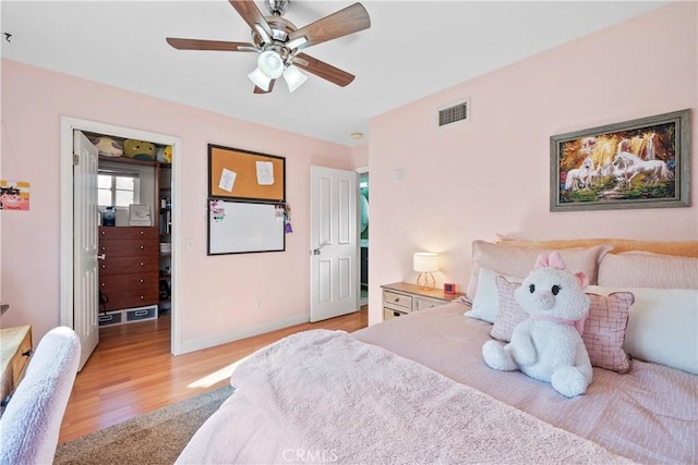 bedroom featuring ceiling fan, a walk in closet, and light wood-type flooring