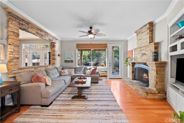 living room with a fireplace, ornamental molding, ceiling fan, and light wood-type flooring