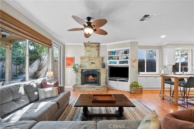 living room with crown molding, a stone fireplace, sink, and light wood-type flooring