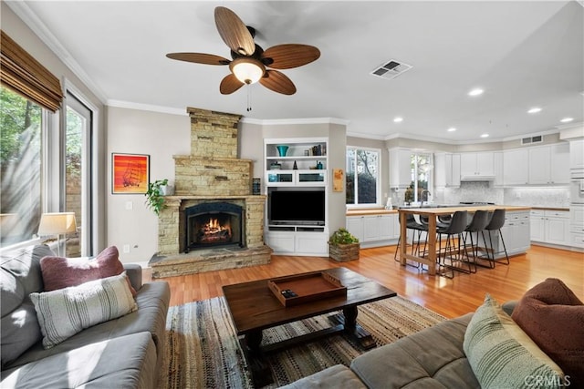 living room featuring crown molding, a stone fireplace, sink, and light hardwood / wood-style flooring