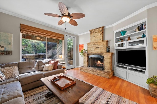 living room with crown molding, ceiling fan, a stone fireplace, and hardwood / wood-style floors