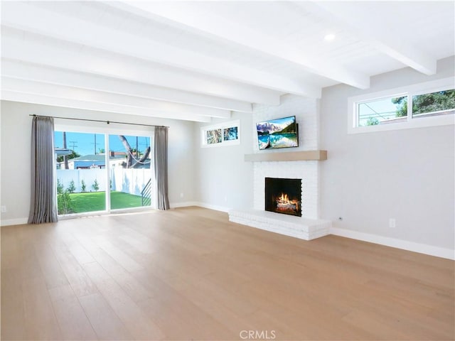 unfurnished living room featuring a brick fireplace, beam ceiling, plenty of natural light, and hardwood / wood-style flooring