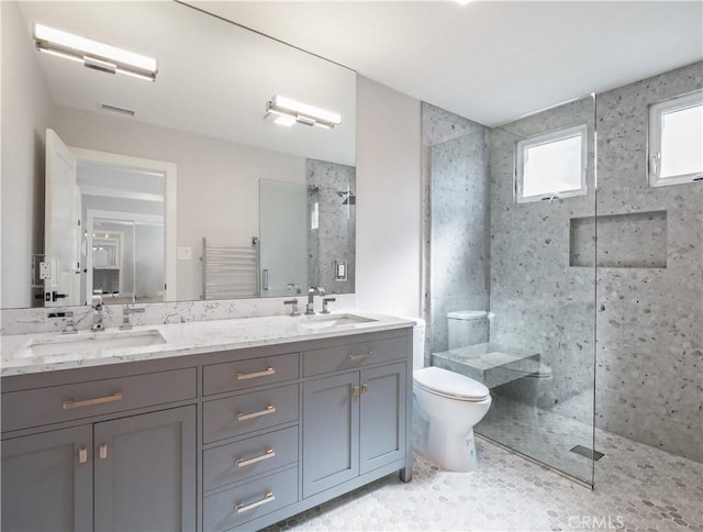 bathroom with tiled shower, vanity, and toilet