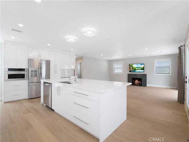 kitchen with sink, white cabinetry, light hardwood / wood-style flooring, appliances with stainless steel finishes, and a kitchen island with sink