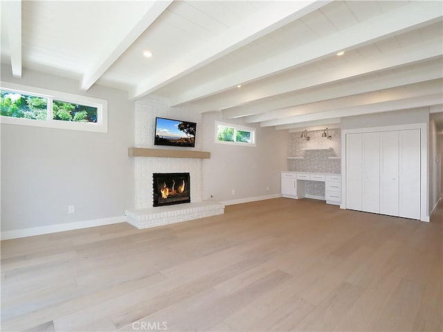 unfurnished living room with a brick fireplace, beamed ceiling, and light wood-type flooring