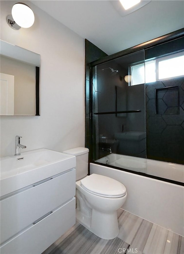 full bathroom with hardwood / wood-style flooring, vanity, combined bath / shower with glass door, and toilet