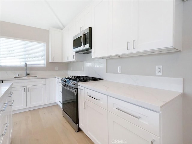 kitchen with white cabinetry, stainless steel appliances, light stone countertops, and sink