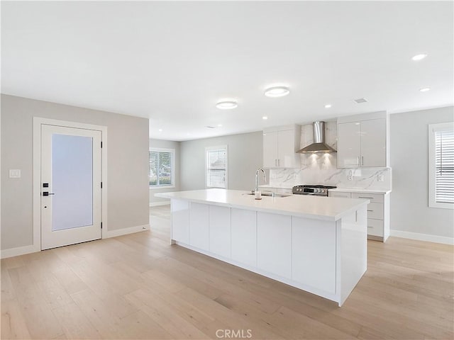 kitchen featuring wall chimney exhaust hood, stainless steel gas range, sink, a center island with sink, and white cabinets