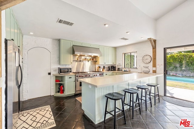 kitchen featuring green cabinetry, wall chimney exhaust hood, stainless steel appliances, and kitchen peninsula