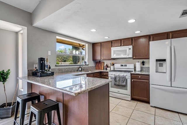 kitchen featuring light stone countertops, a breakfast bar, white appliances, and kitchen peninsula