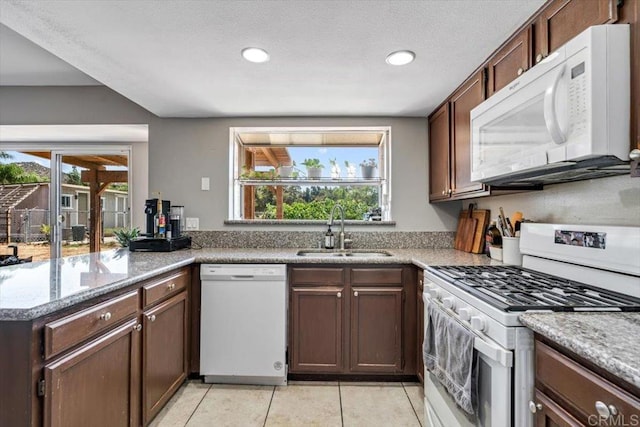 kitchen featuring light tile patterned flooring, sink, dark brown cabinetry, kitchen peninsula, and white appliances