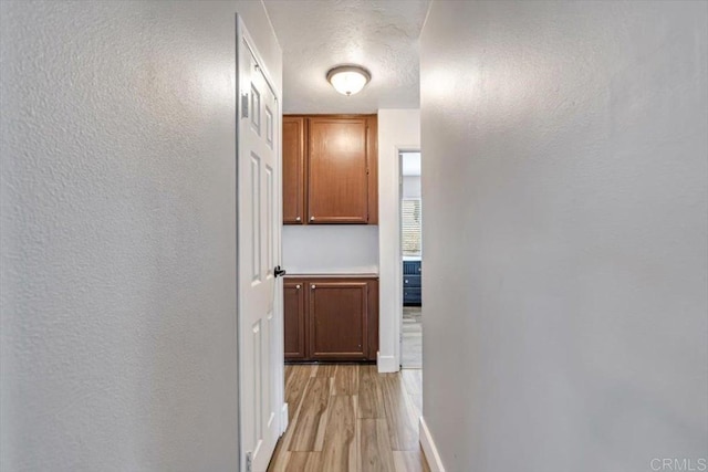 corridor featuring light wood-style flooring, a textured wall, and a textured ceiling