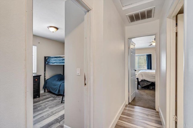 hall featuring visible vents, baseboards, and wood finished floors