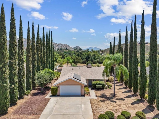 view of front of house featuring a mountain view, roof mounted solar panels, an attached garage, and driveway