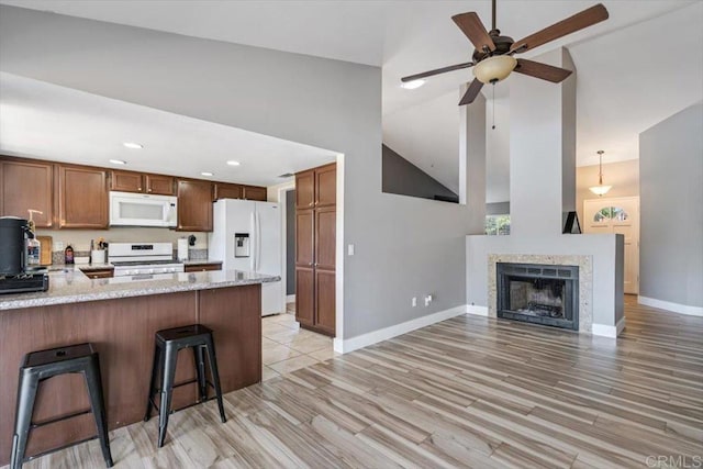 kitchen with a kitchen bar, white appliances, kitchen peninsula, light stone countertops, and light wood-type flooring