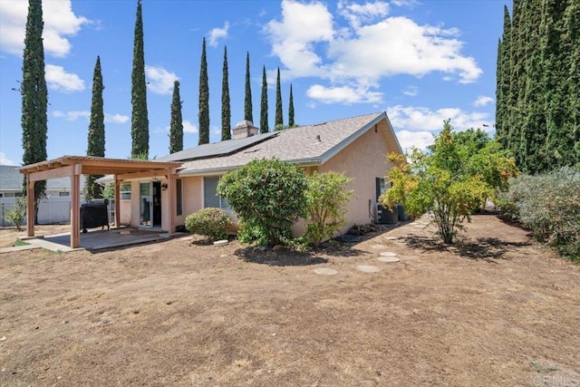 back of property with stucco siding, a patio, fence, solar panels, and a chimney