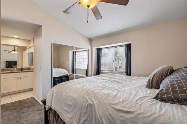 bedroom with light tile patterned floors, lofted ceiling, a closet, ensuite bathroom, and light carpet