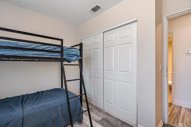 unfurnished bedroom featuring wood finished floors, visible vents, a closet, and baseboards