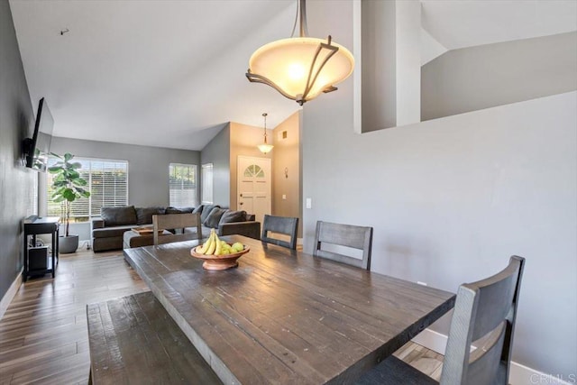 dining area featuring wood finished floors, baseboards, and high vaulted ceiling