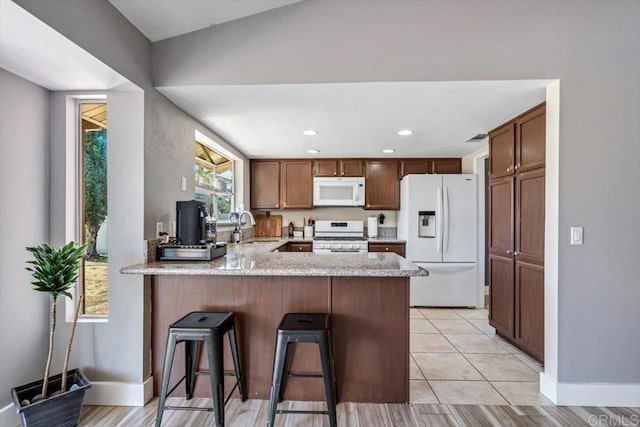 kitchen with a sink, a kitchen breakfast bar, white appliances, a peninsula, and light tile patterned floors