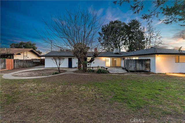 back house at dusk featuring a yard and a patio area