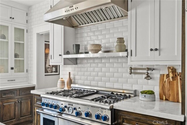 kitchen featuring dark brown cabinetry, wall chimney exhaust hood, white cabinetry, range with two ovens, and backsplash