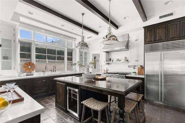 kitchen with beamed ceiling, sink, backsplash, stainless steel appliances, and wall chimney exhaust hood