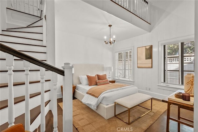 bedroom featuring wood-type flooring, a towering ceiling, and a notable chandelier